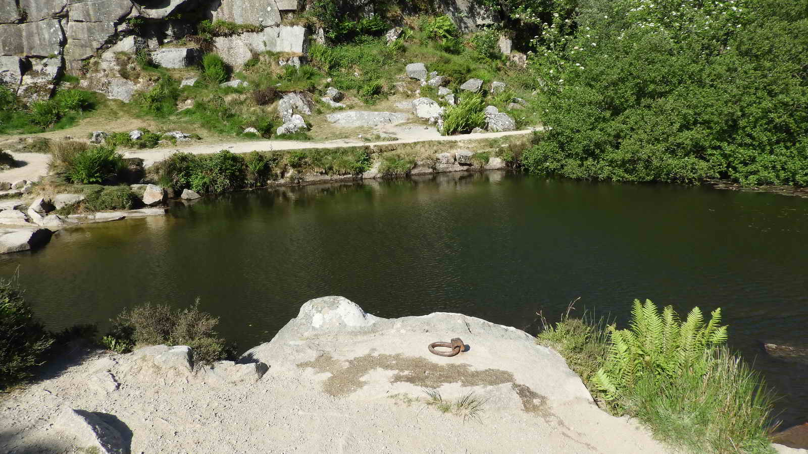 A view across the flooded deep pit showing the near-side iron ring in the foreground and the second ring on the larger “white” rock straight across the water